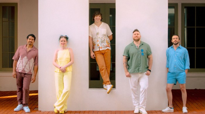 Five people stood against a white wall wearing brightly coloured clothes