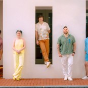 Five people stood against a white wall wearing brightly coloured clothes