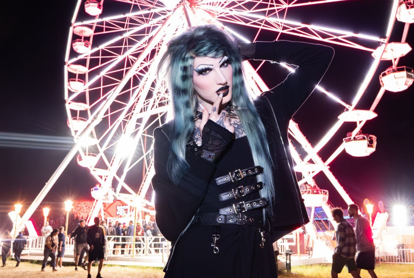 electronic artist 6arely humanposing in front of a light up ferris wheel at night