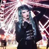 electronic artist 6arely humanposing in front of a light up ferris wheel at night