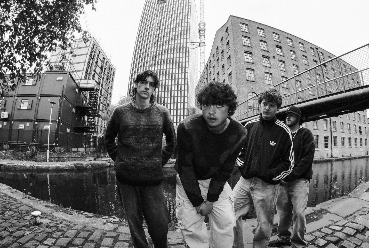 Black and white image Manchester band Arkayla, the four members are stood in front of a canal near some high rise buildings