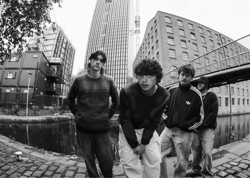 Black and white image Manchester band Arkayla, the four members are stood in front of a canal near some high rise buildingsx