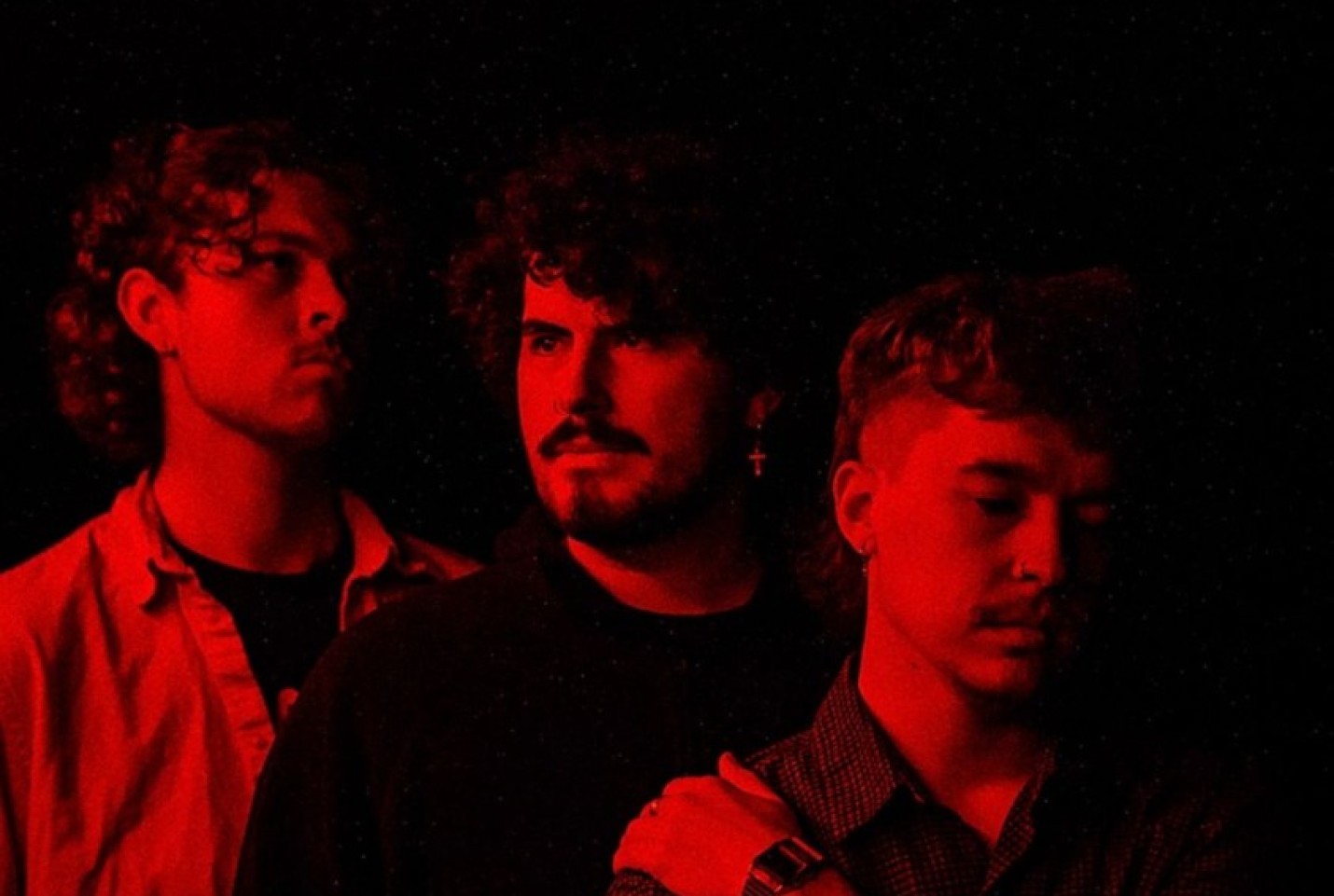 Ample House members looking into the distance with a red light reflecting onto their faces.