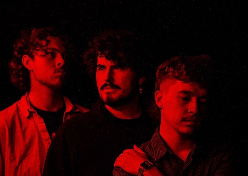 Ample House members looking into the distance with a red light reflecting onto their faces.x