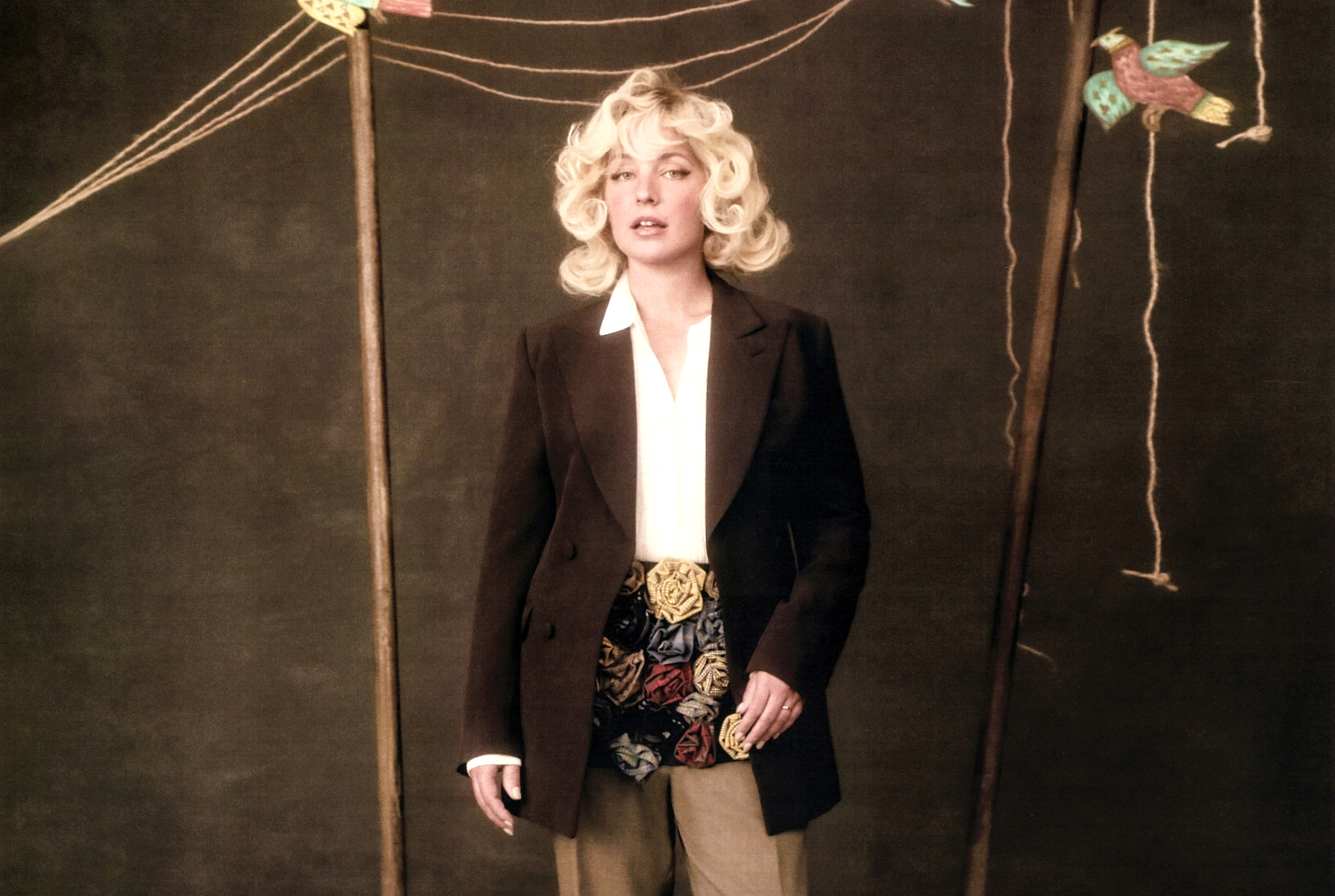 Girl with blonde short, curly hair, standing against brown background