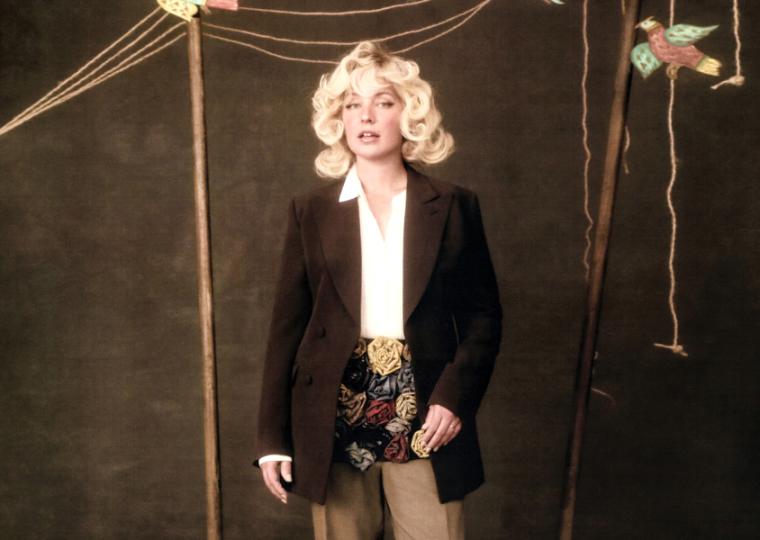 Girl with blonde short, curly hair, standing against brown backgroundx