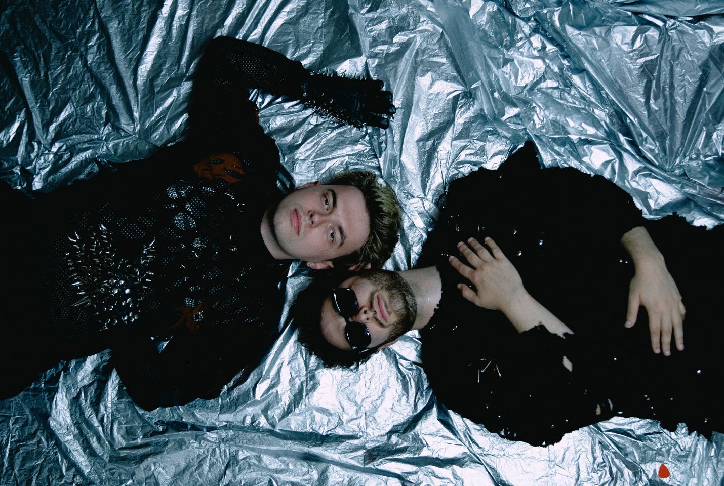 Two men dressed in black laying on a silver sheet