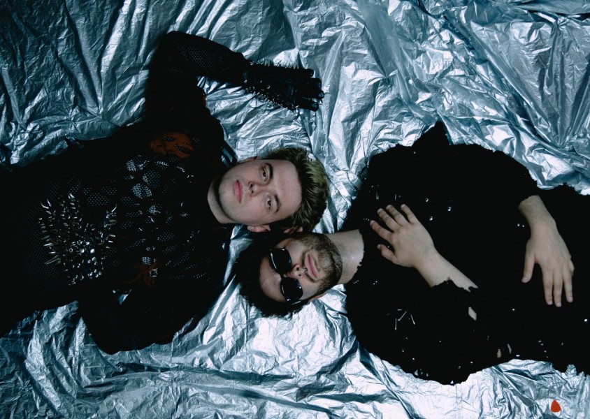 Two men dressed in black laying on a silver sheetx