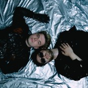 Two men dressed in black laying on a silver sheet
