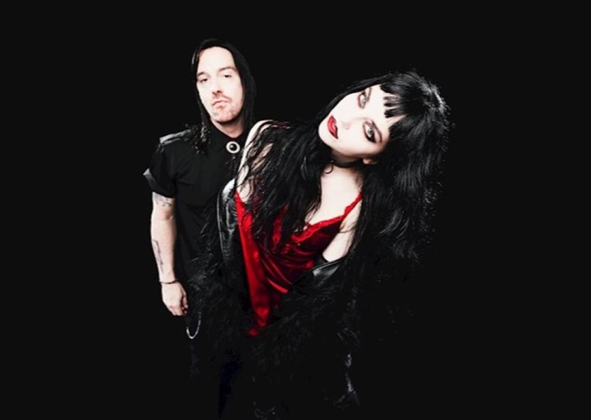 man and woman both with black hair and dark clothes with dark backgroundx