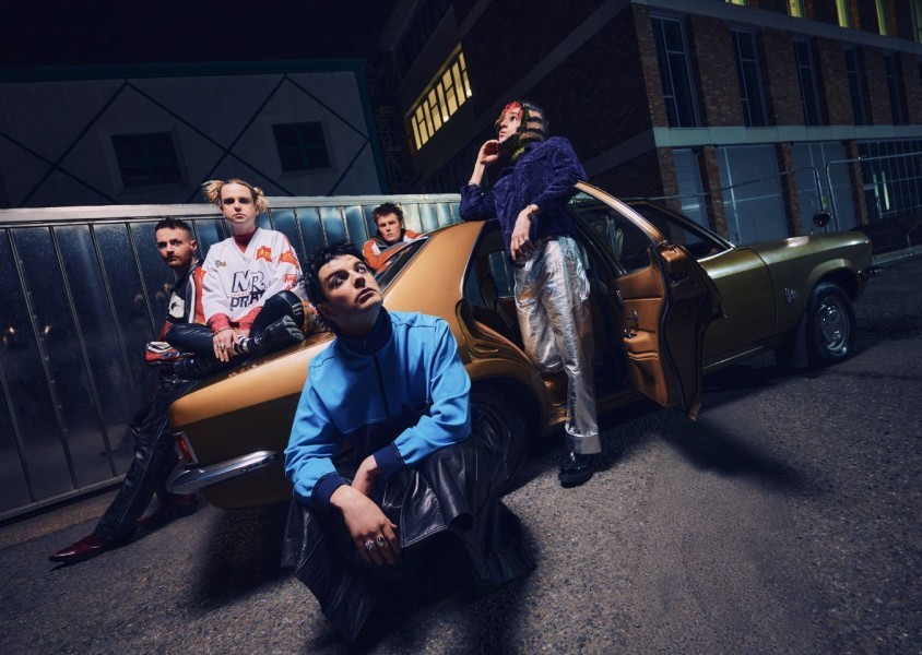 The members of Fontaines D.C., Grian Chatten, Connor Curley Conner Deegan, Carols O'Connell and Tom Coll posing in front of a car.x