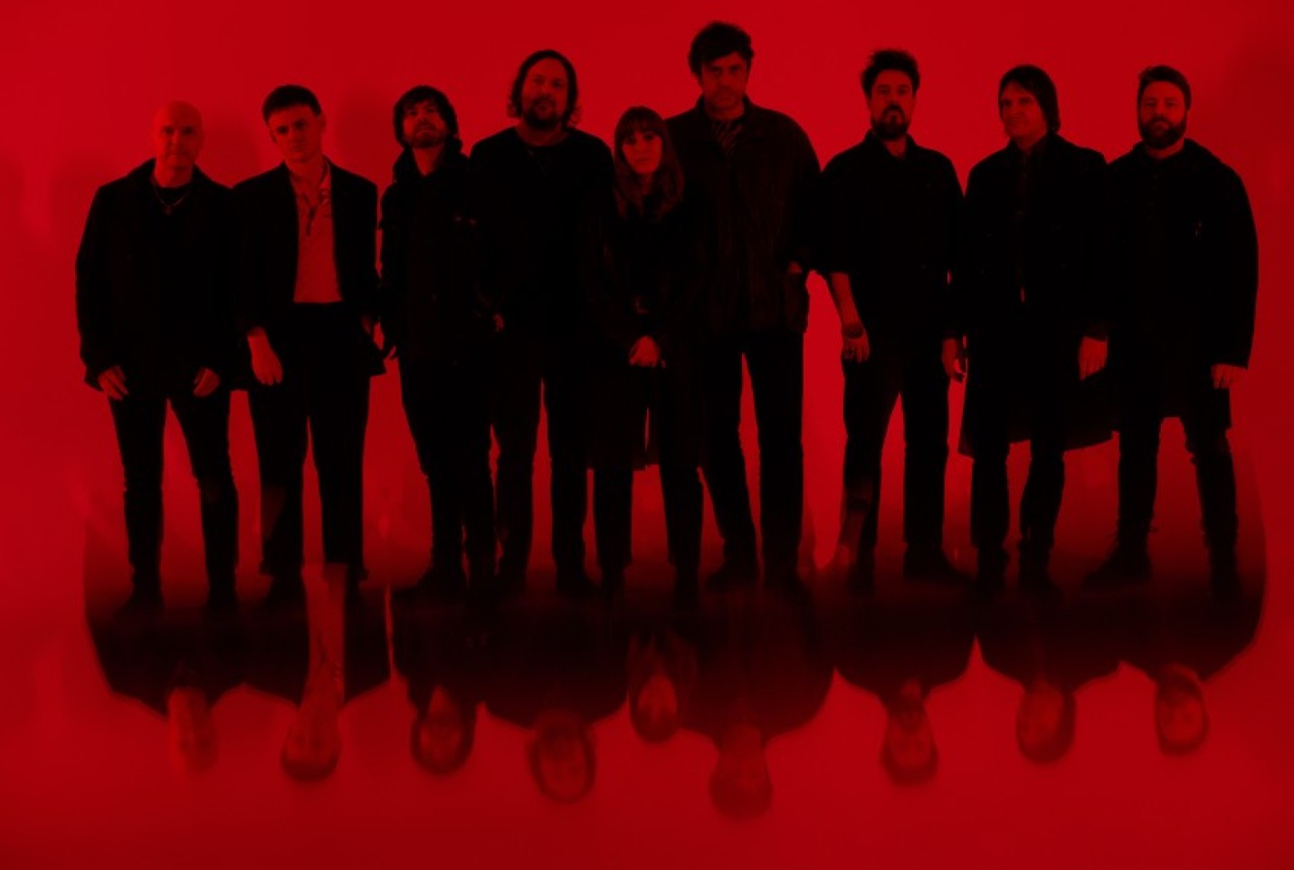 The band Helicon members looking into the camera while in front of a red back drop. 