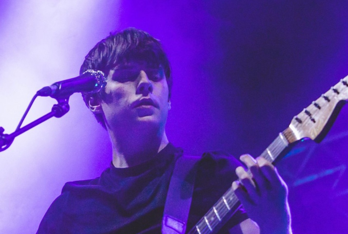 Jake Bugg on stage playing the guitar with a purple lights shining on him.