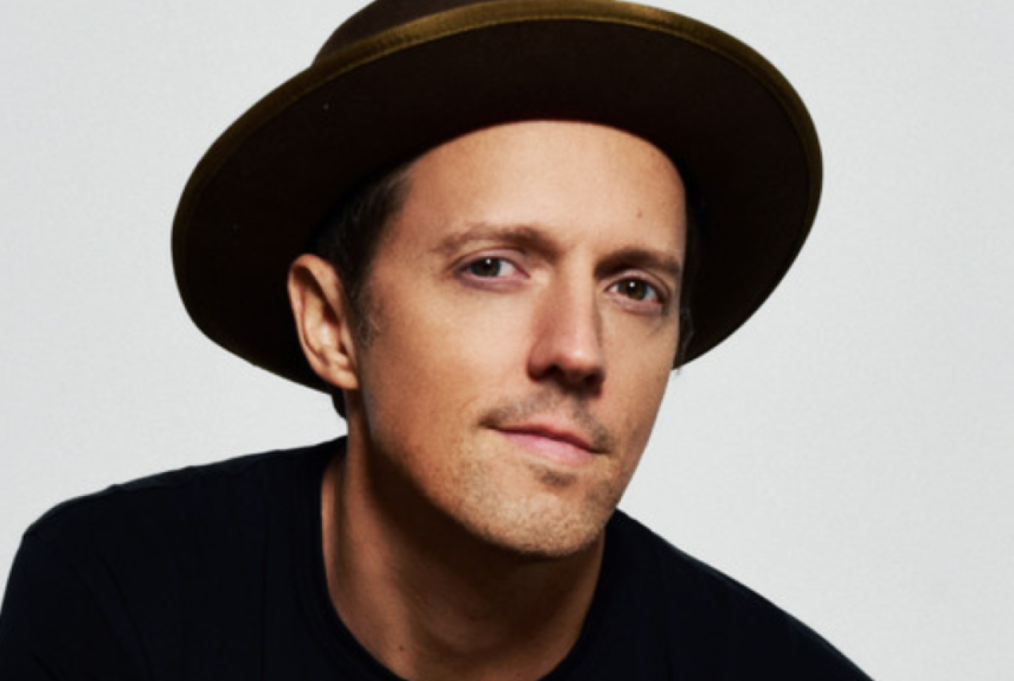 Jason Mraz wearing a hat looking into the camera with a white backdrop behind him 