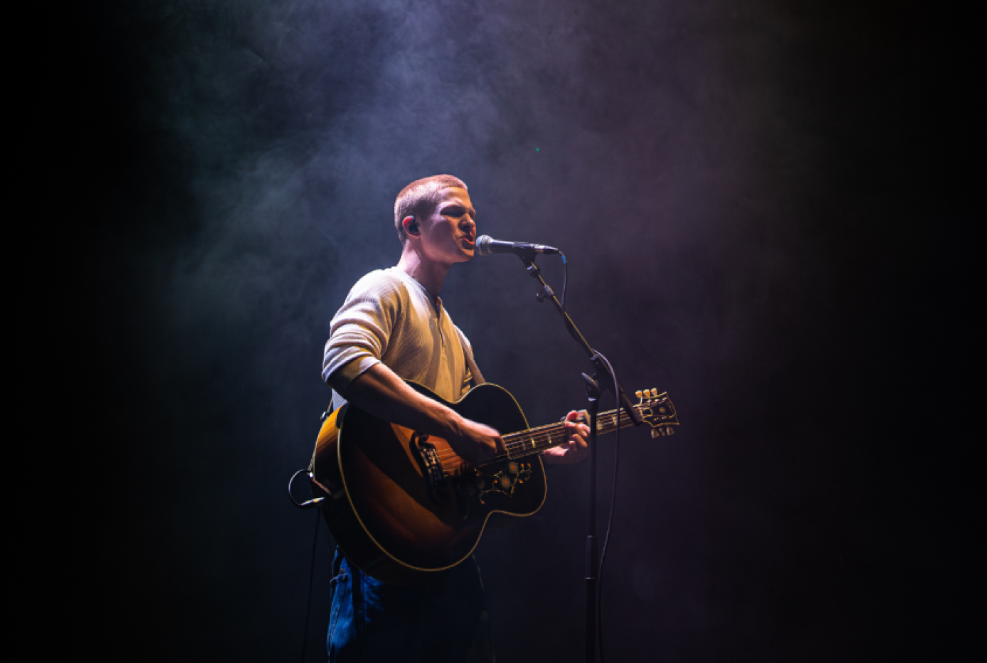 Jasper Hodges singing into a microphone and playing the guitar.