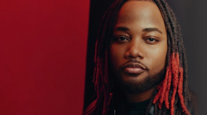 Leon Thomas looking into the camera with a red and black background behind him.