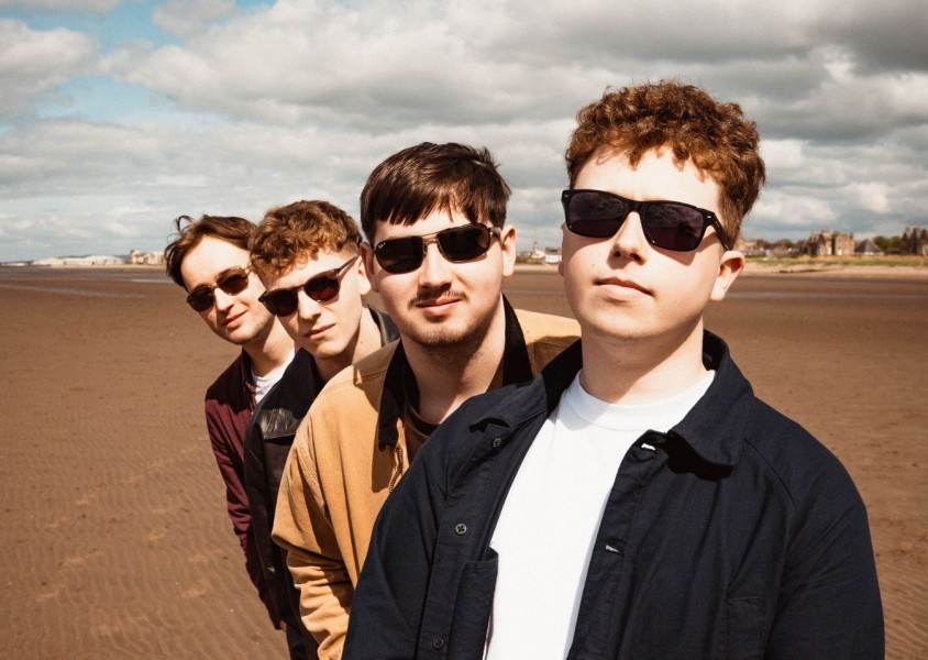 Mixed Signals members Ben Gardiner, James Armstrong, Leon Calder and Nathan Christie standing on a beach, smiling into the camera.x