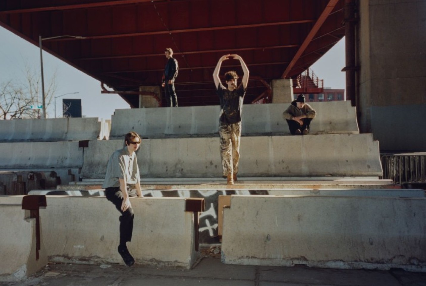 The Model/Actriz, with members standing in between cement walls looking at the camera