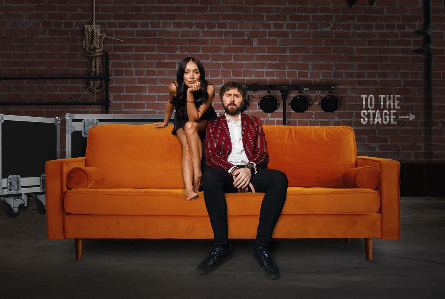 A woman and man sat backstage on an orange sofa