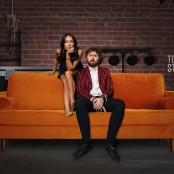 A woman and man sat backstage on an orange sofa
