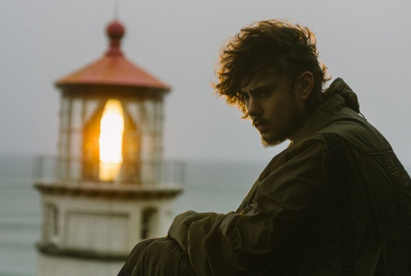 Quadeca sitting looking into the distance with a lighthouse behind him 