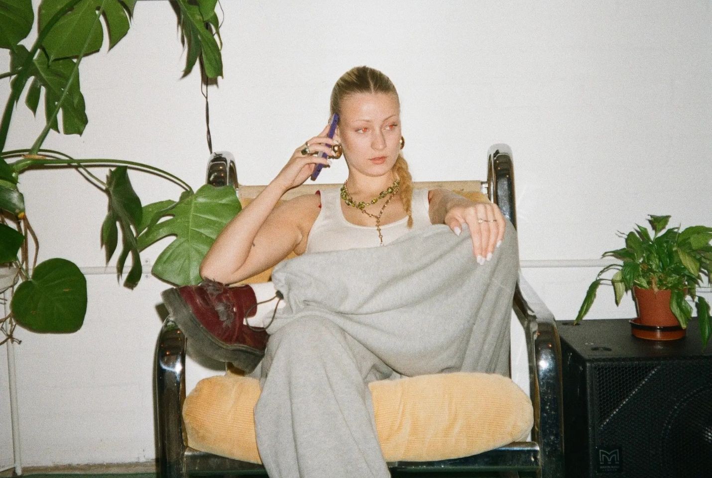 Girl sat down on a chait on the phone next to a plant