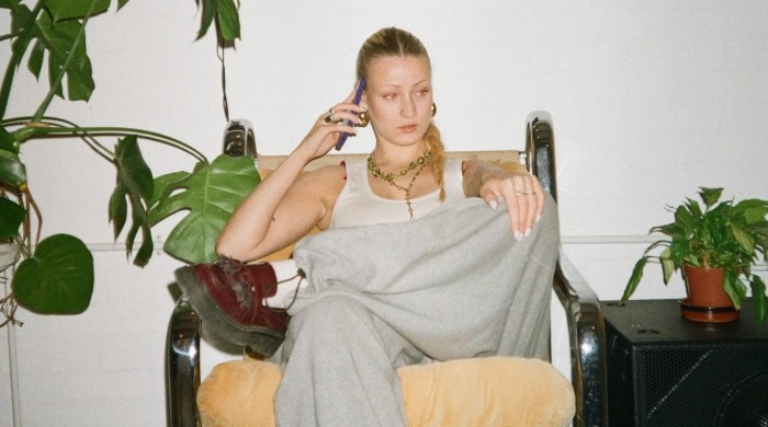 Girl sat down on a chait on the phone next to a plant