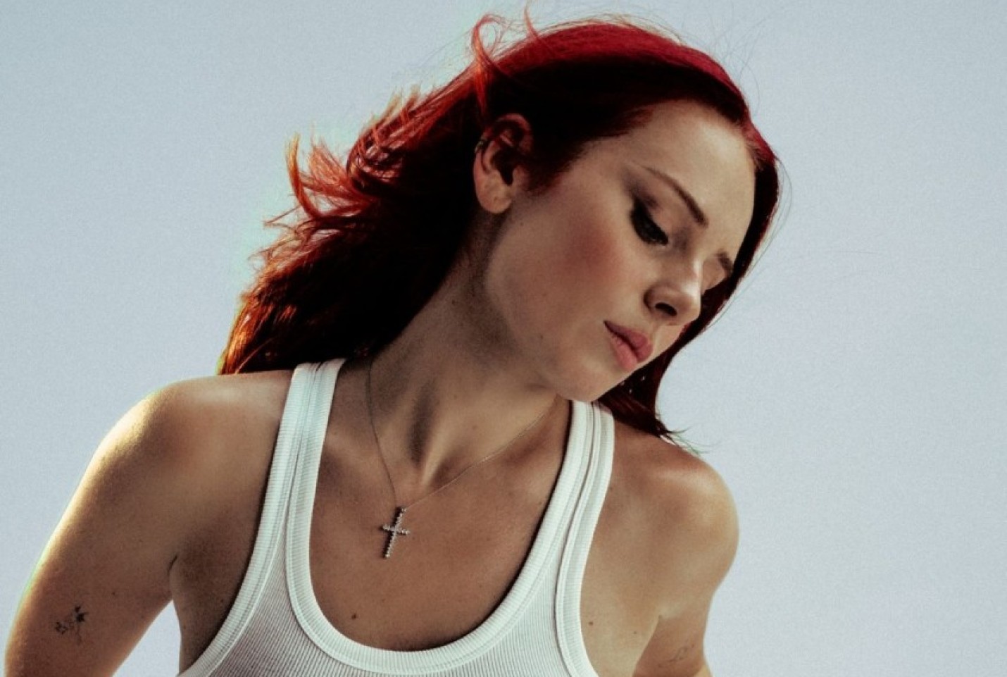 Rose Gray wearing a white tank top and tilting her head to the left with her eyes closed.