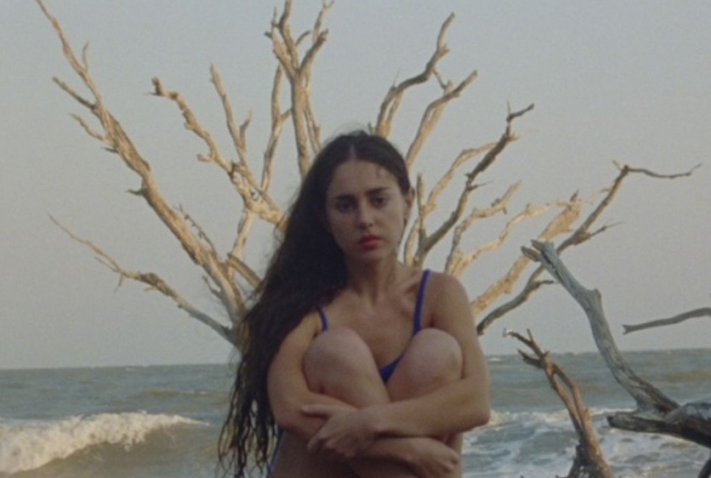 Samia sitting with her knees up to her chest on a beach.