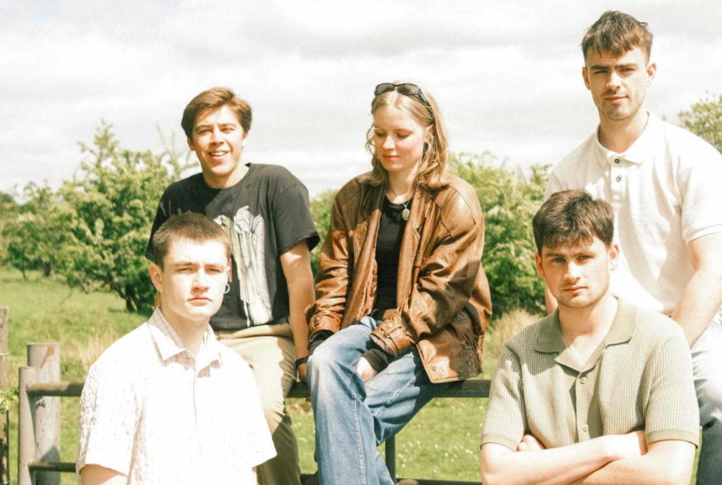 The band Solasta with the members sitting on a fence and smiling at the camera with trees behind them.