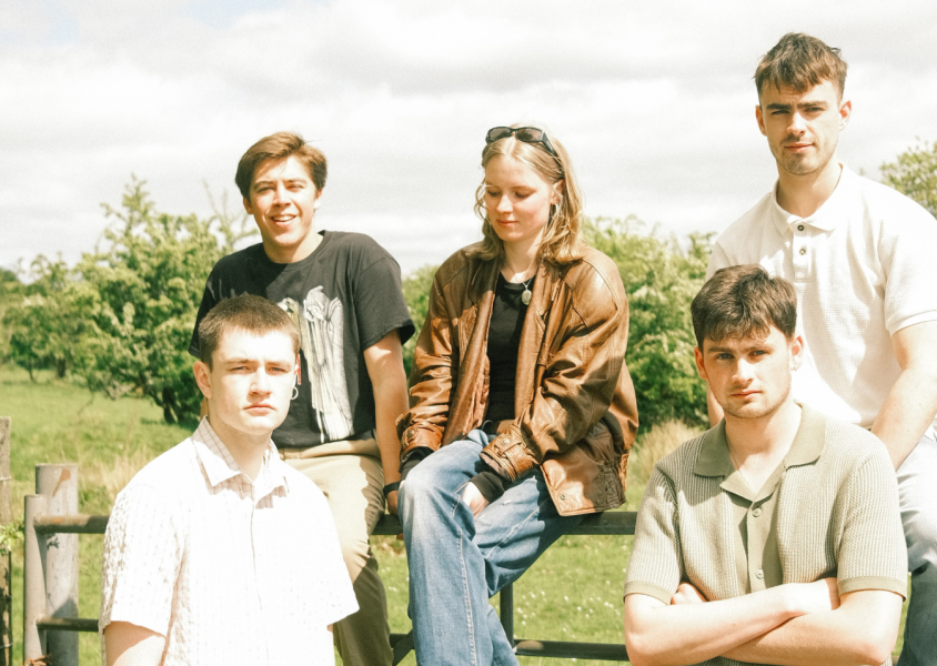 The band Solasta with the members sitting on a fence and smiling at the camera with trees behind them.x