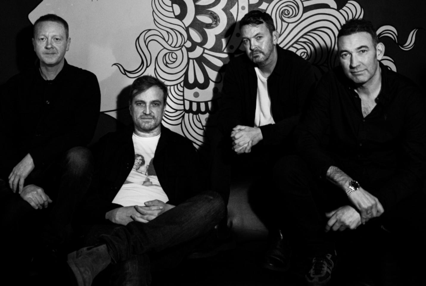 The band Starsailor, with members Barry Westhead, Ben Byrne, James Stelfox and James Walsh sitting on a couch smiling at the camera.