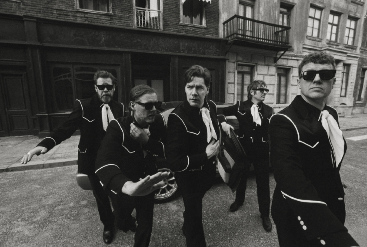 The hives band looking into the distance, while stood around a car.