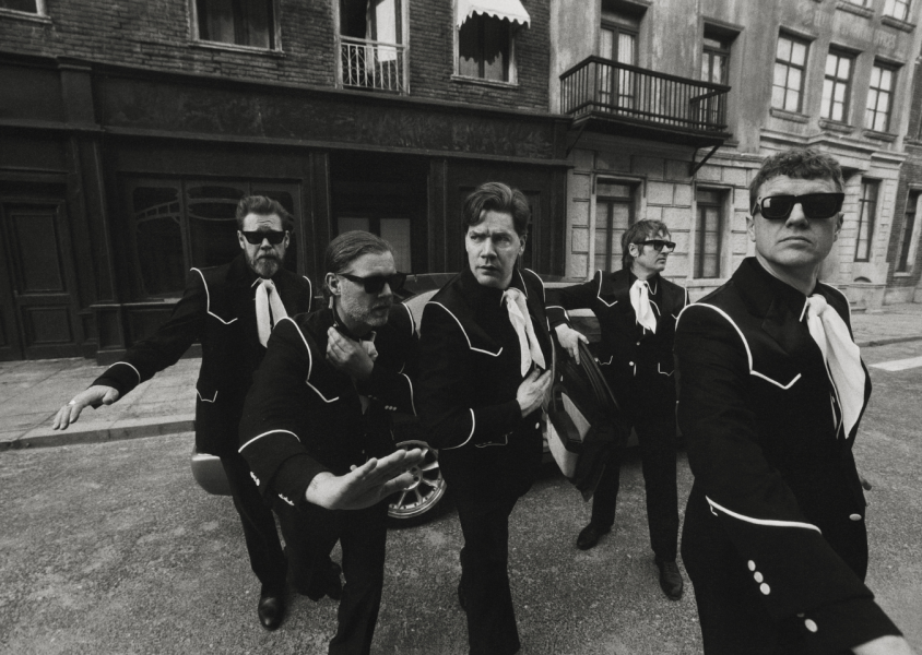 The hives band looking into the distance, while stood around a car.