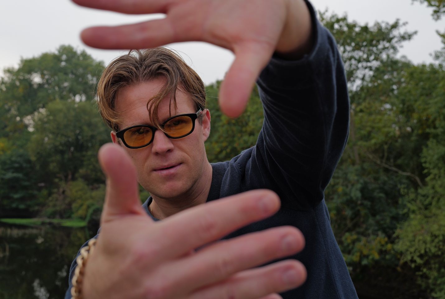 A man with blonde hair wearing orange lensed glasses and a blue jumper