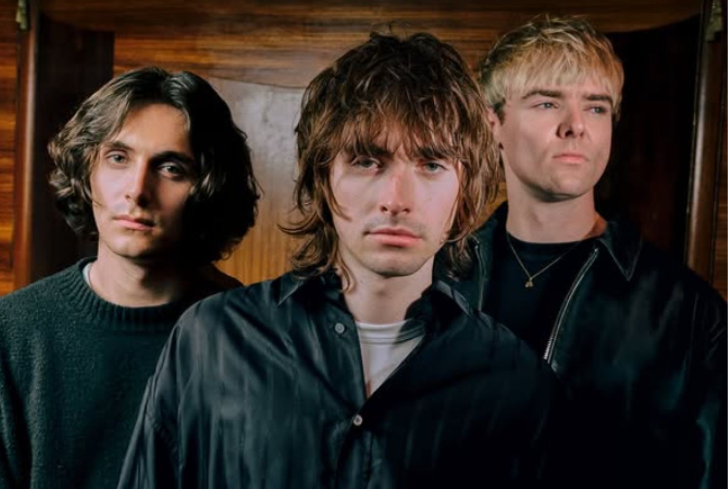 Three men dressed in black stand in front of a wooden clad wall
