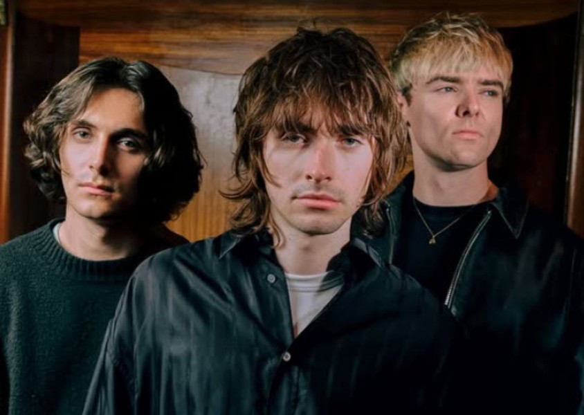 Three men dressed in black stand in front of a wooden clad wallx