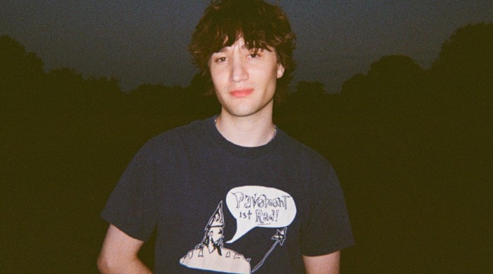 A man with messy brown hair wearing a navy tshirt and silver chain