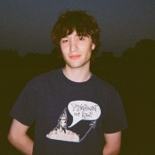 A man with messy brown hair wearing a navy tshirt and silver chain