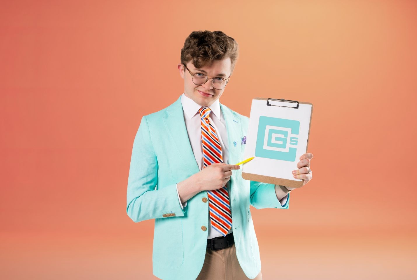 A man wearing a white shirt, brown trouser, a light blue jacket, striped tie and glasses holding a clip board and yellow pen standing in front of an orange backdrop