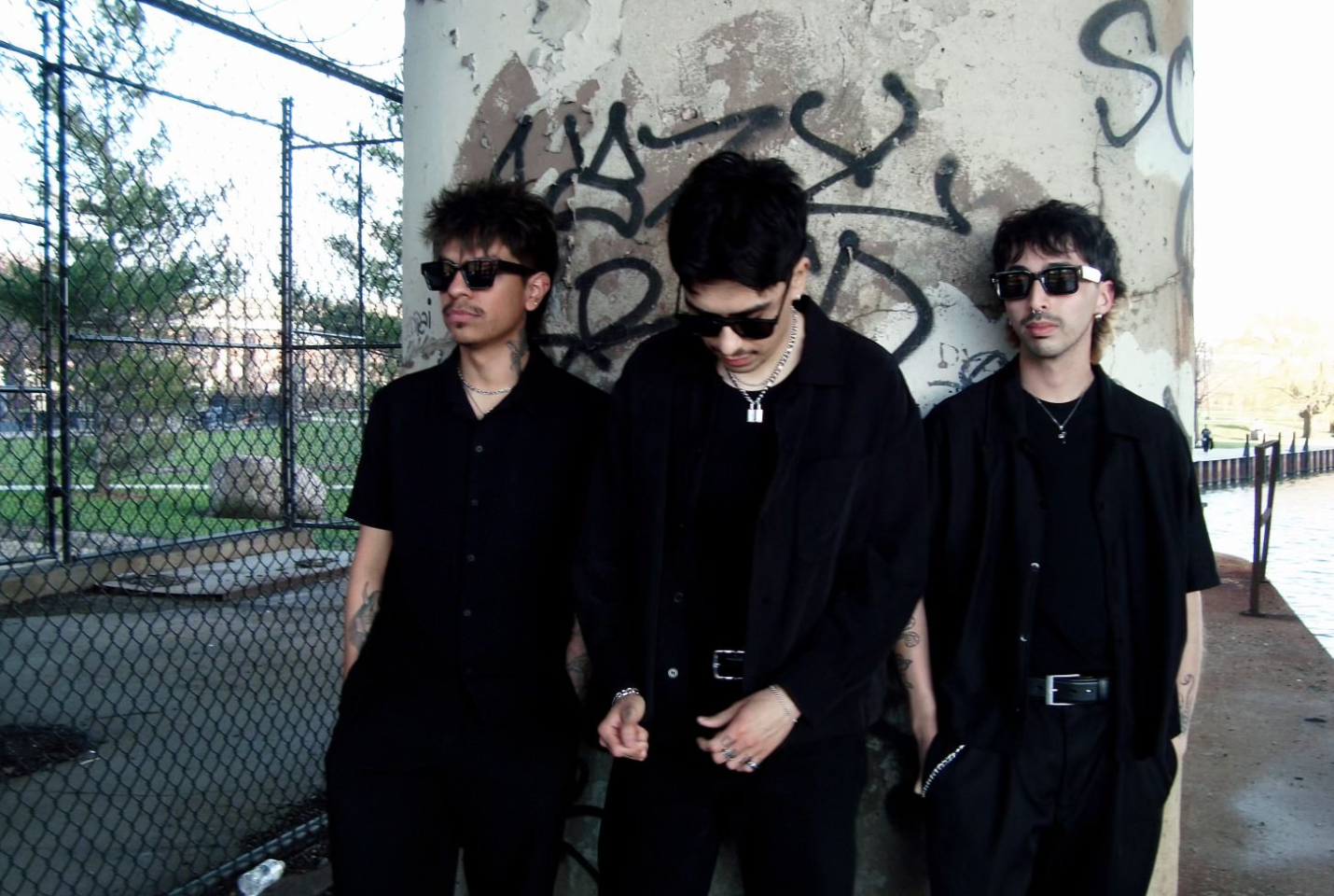 3 men posing against wall with graffiti wearing sunglasses