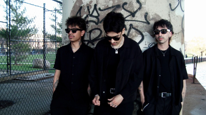 3 men posing against wall with graffiti wearing sunglasses