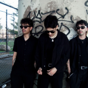 3 men posing against wall with graffiti wearing sunglasses