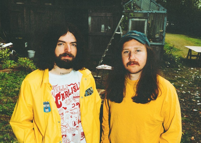 Two men dressed in yellow stood in a gardenx