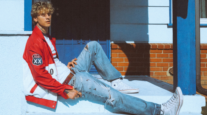 Man sitting on a step wearing a red baseball jacket and blue jeans