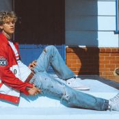 Man sitting on a step wearing a red baseball jacket and blue jeans 