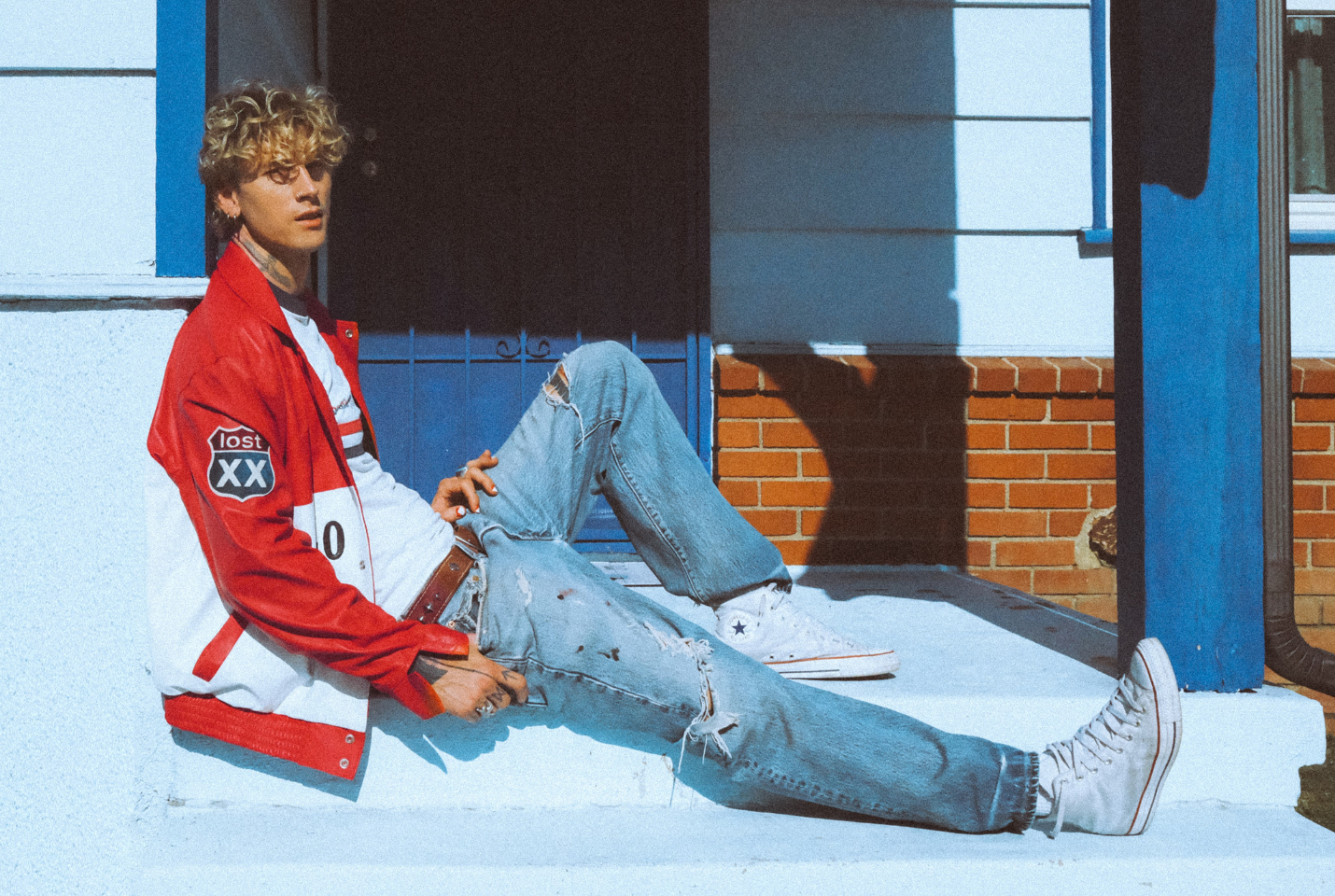 Man sitting on a step wearing a red baseball jacket and blue jeans