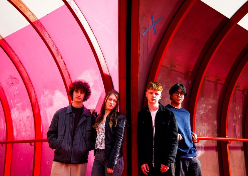 The Grapevine band, with members standing in a pink tunnel, looking at the camera with straight faces.x