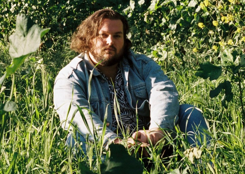 Tyler Ballgame sitting in a field smiling at the camera.x
